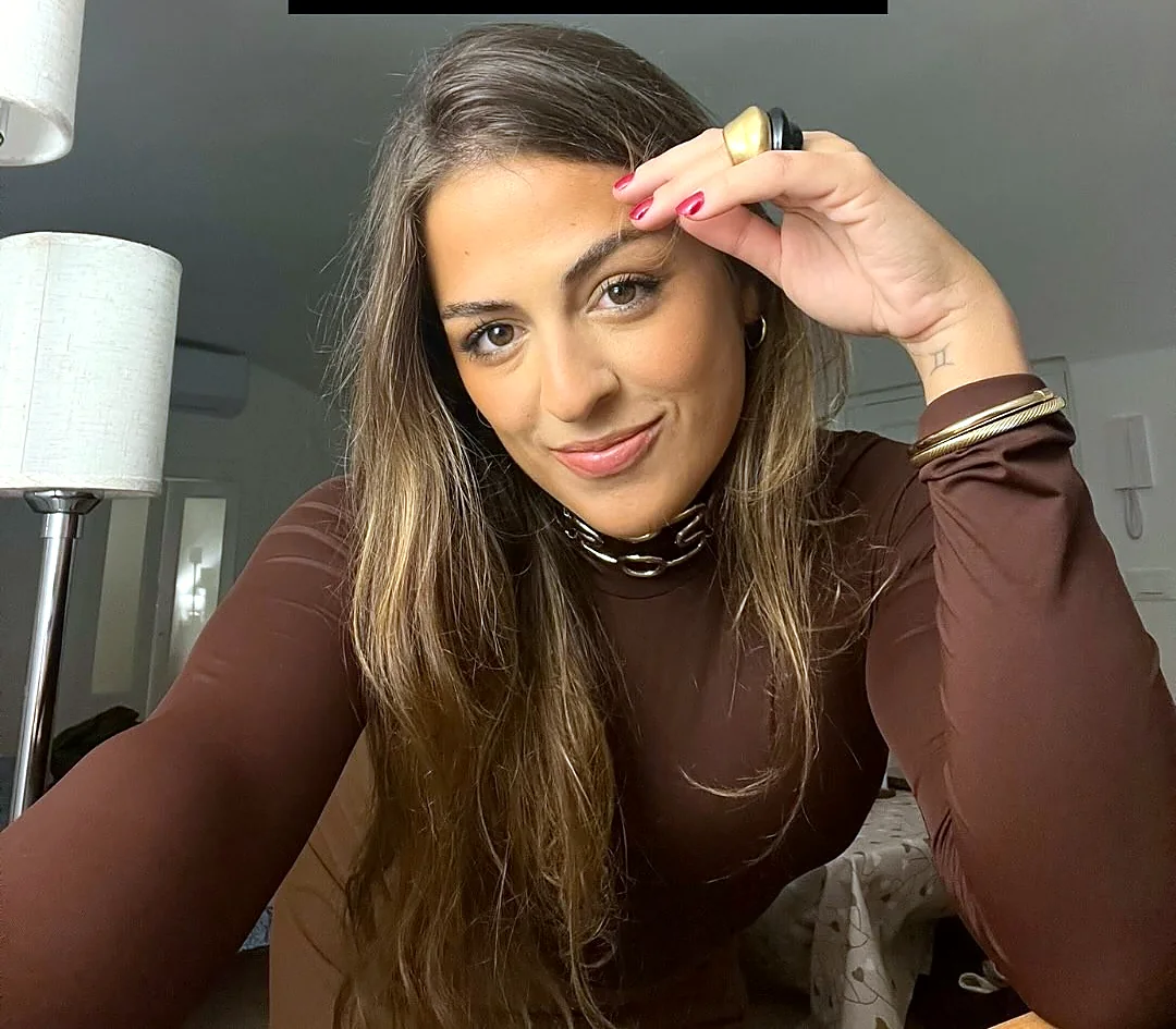 Stefania sorrindo, de blusa marrom, com a mão na cabeça