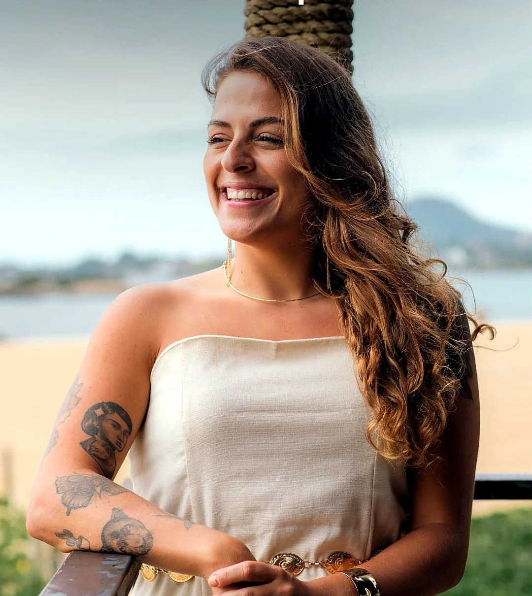Stefania sorrindo, de blusa branca, com o mar ao fundo