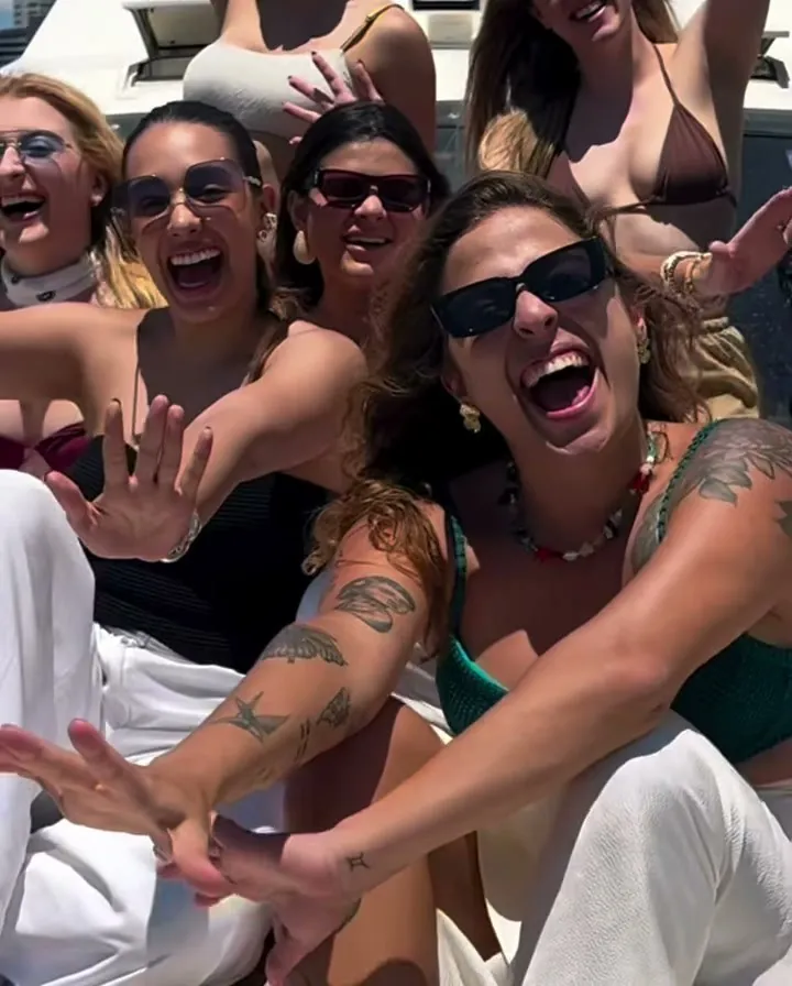 Stefania com alunas social medias num barco, rindo e acenando